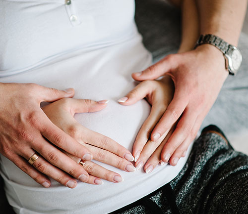 Hände formen ein Herz vor dem Bauch einer Schwangeren