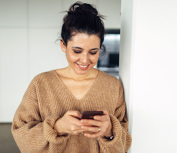 Ohne Qualm und Alkohol durch die Schwangerschaft? Auch das Handy kann helfen! Lächelnde Frau tippt auf ein Smartphone
